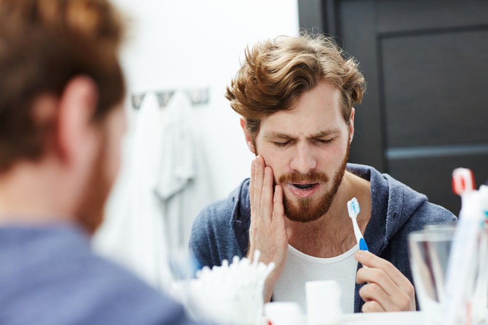 Man brushing his teeth while experiencing tooth pain.